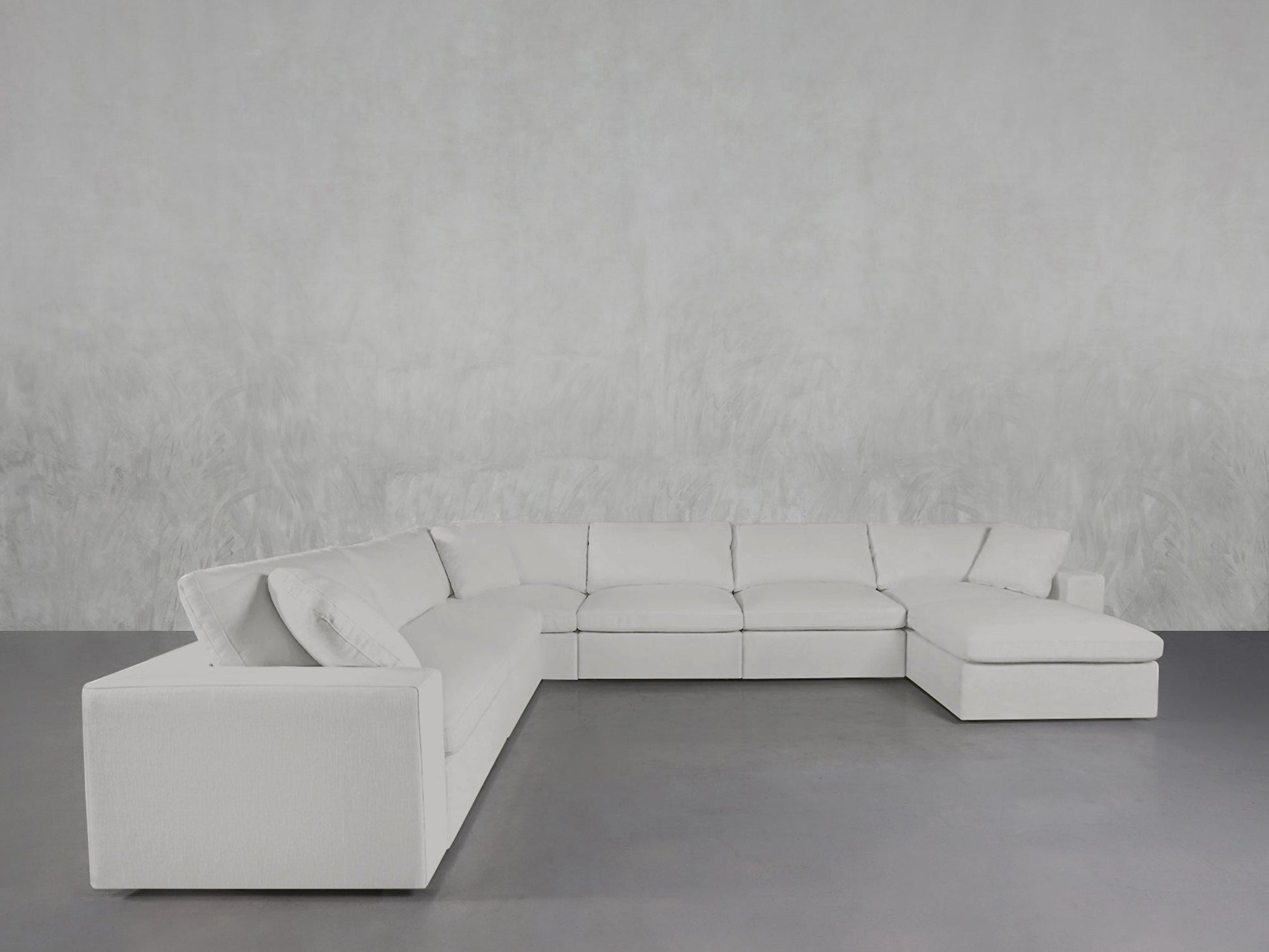 A 7-Seat Modular Chaise Corner Sectional in modern white is placed against a light gray textured wall on a smooth gray floor in a minimalist room.