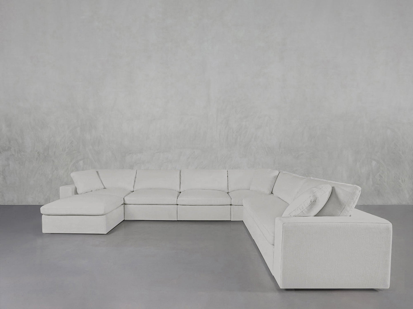 The 7-Seat Modular Chaise Corner Sectional, featuring a modern white design and left-side chaise lounge, sits against a light gray textured wall on a smooth gray floor.