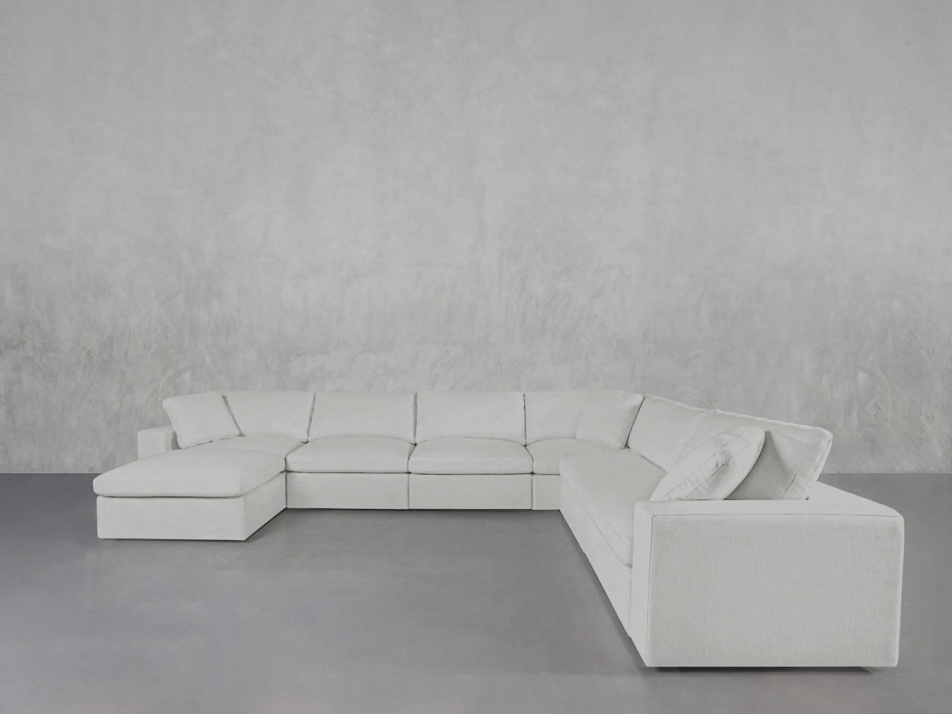 The 7-Seat Modular Chaise Corner Sectional, featuring a modern white design and left-side chaise lounge, sits against a light gray textured wall on a smooth gray floor.