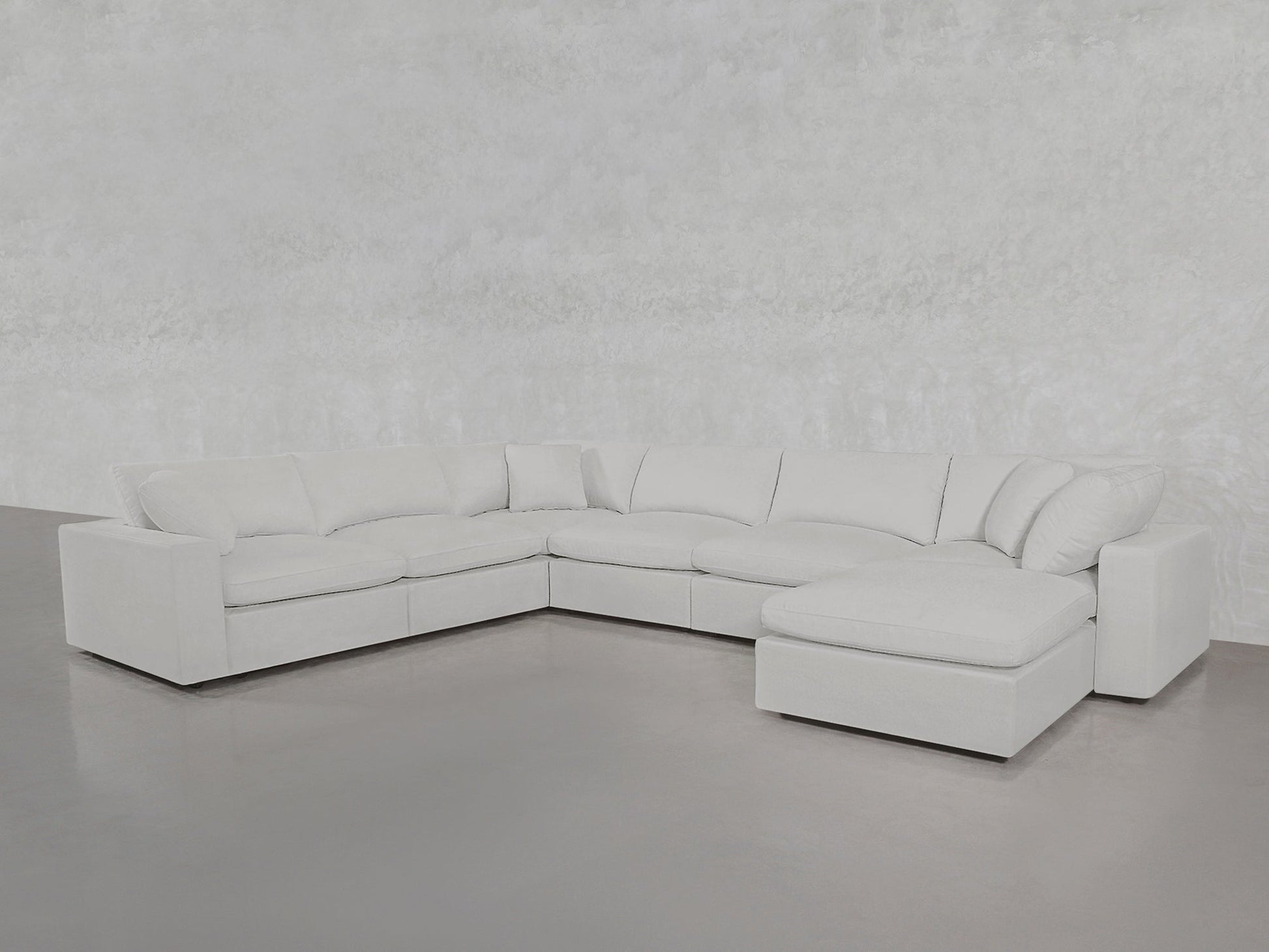 The 7-Seat Modular Chaise Corner Sectional, featuring multiple seat and back cushions, is showcased in a minimalist room with light gray walls and a smooth gray floor.
