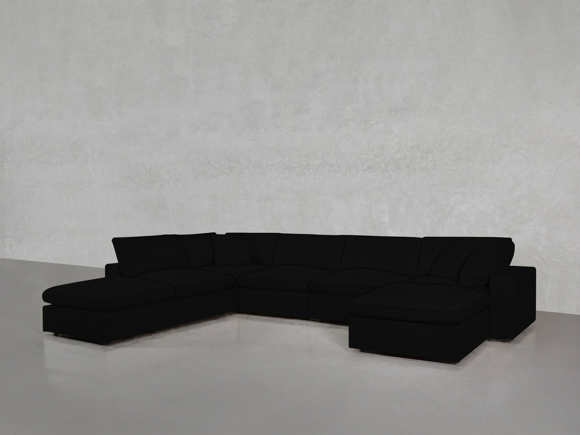 A spacious black 7-Seat Modular Chaise Corner Lounger Sectional with wide seats and no visible legs, placed against a plain light gray wall and floor.