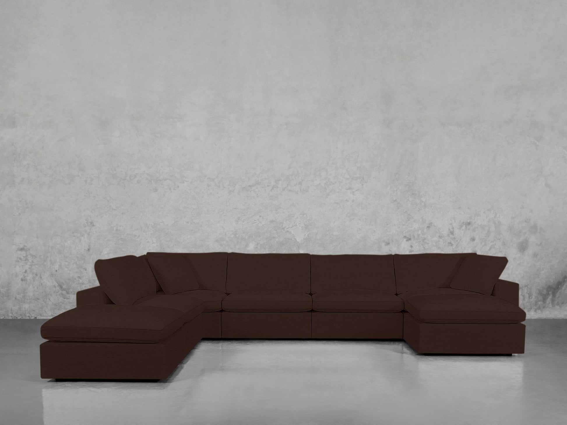 A 7-Seat Modular Chaise Corner Lounger Sectional in dark brown with wide seats and cushions is placed against a plain, light gray textured wall on a shiny, light-colored floor.