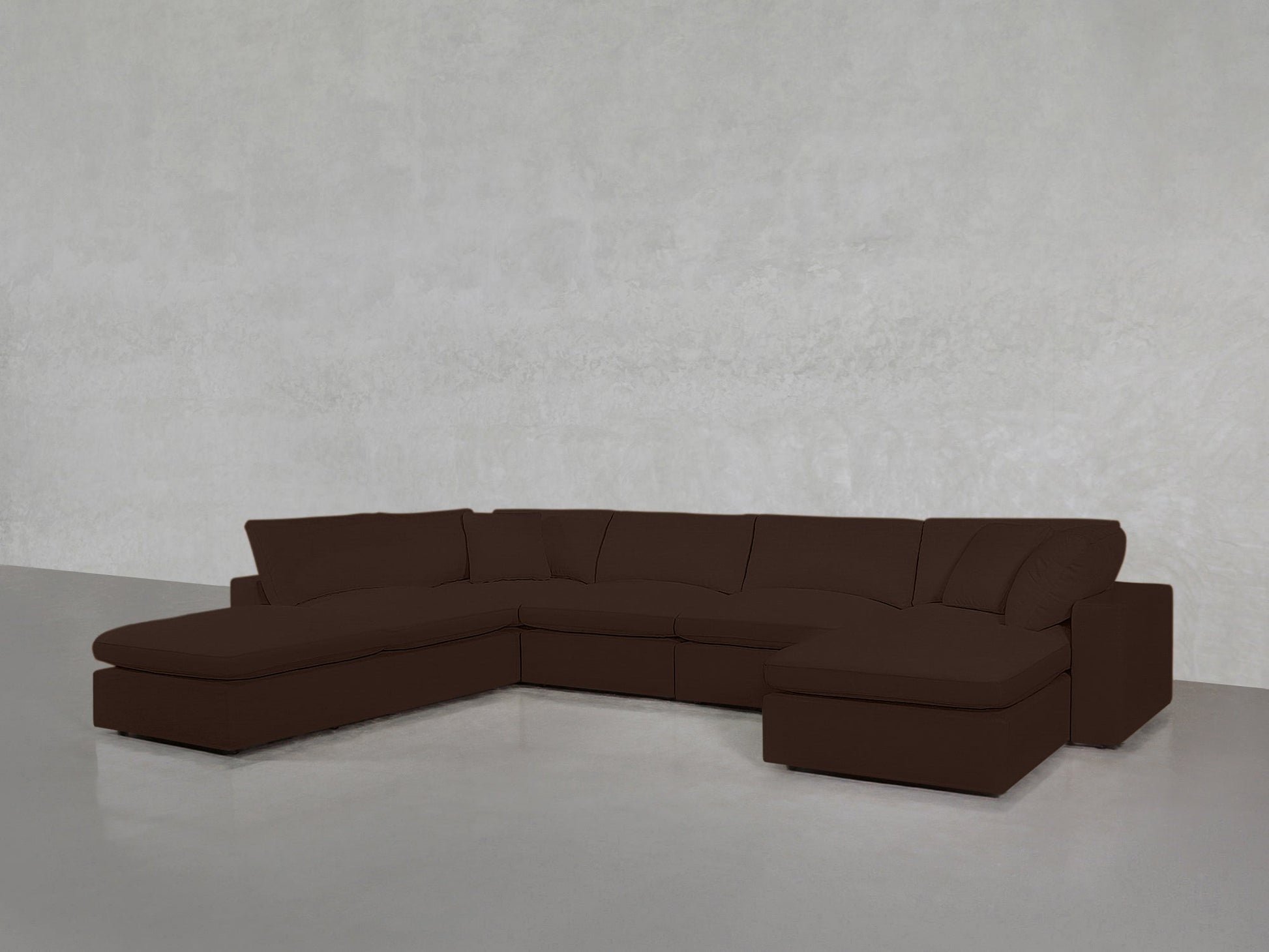 A 7-Seat Modular Chaise Corner Lounger Sectional in dark brown with cushions and a chaise lounge on one end sits on a smooth, light gray floor against a plain light gray wall.