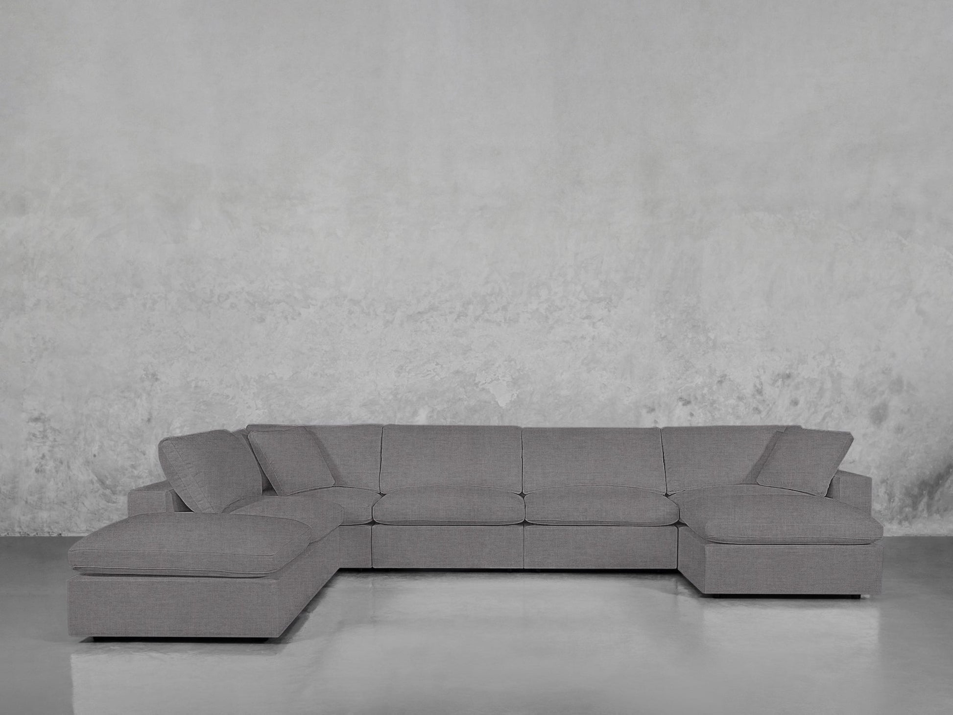 A 7-Seat Modular Chaise Corner Lounger Sectional with clean lines in gray sits on a shiny floor against a textured light gray wall, creating a minimalist, modern look.