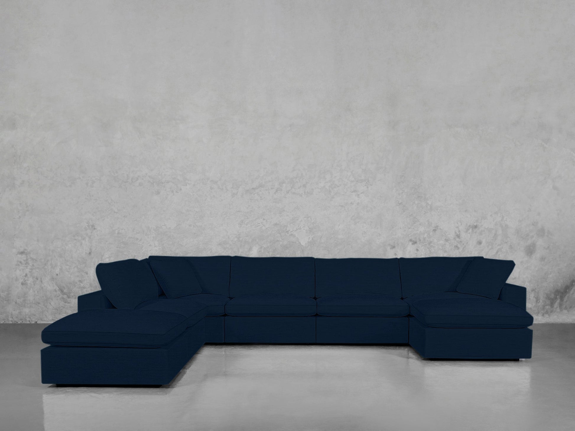The 7-Seat Modular Chaise Corner Lounger Sectional in dark blue stands against a light gray textured wall, its chaise lounges on both ends reflecting subtly off the sleek floor.
