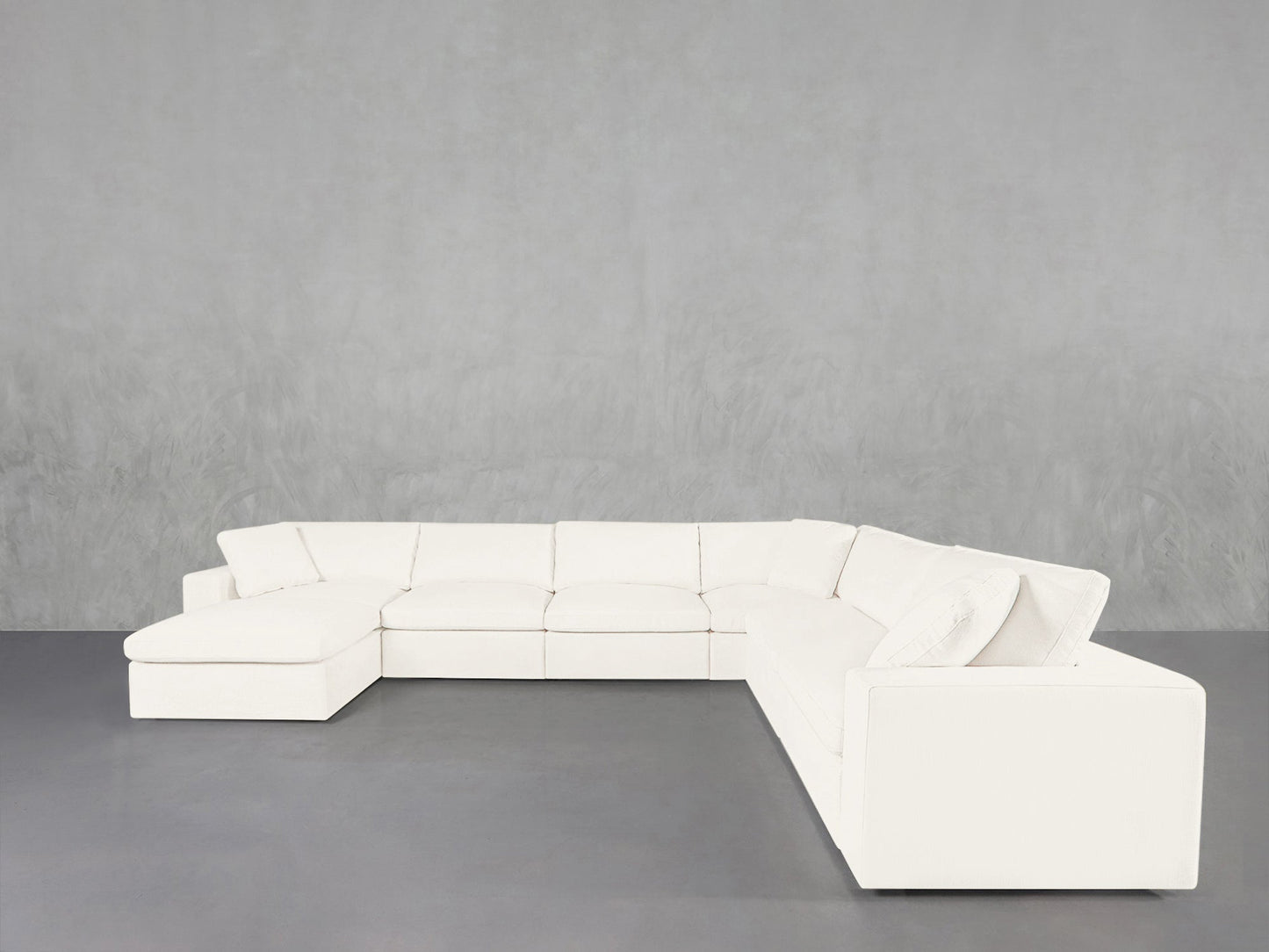 A 7-Seat Modular Chaise Corner Sectional in white L-shape rests against a light gray textured wall on a smooth gray floor.