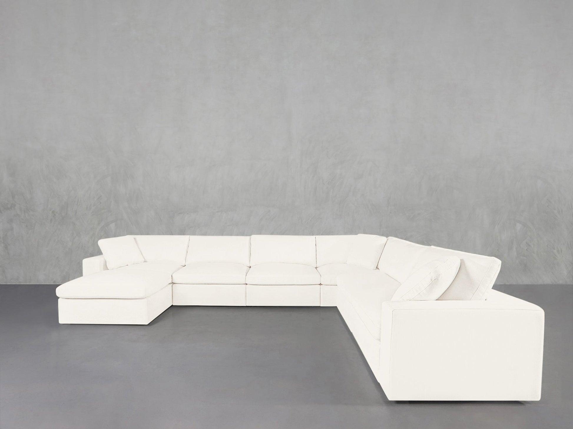 A 7-Seat Modular Chaise Corner Sectional in white L-shape rests against a light gray textured wall on a smooth gray floor.