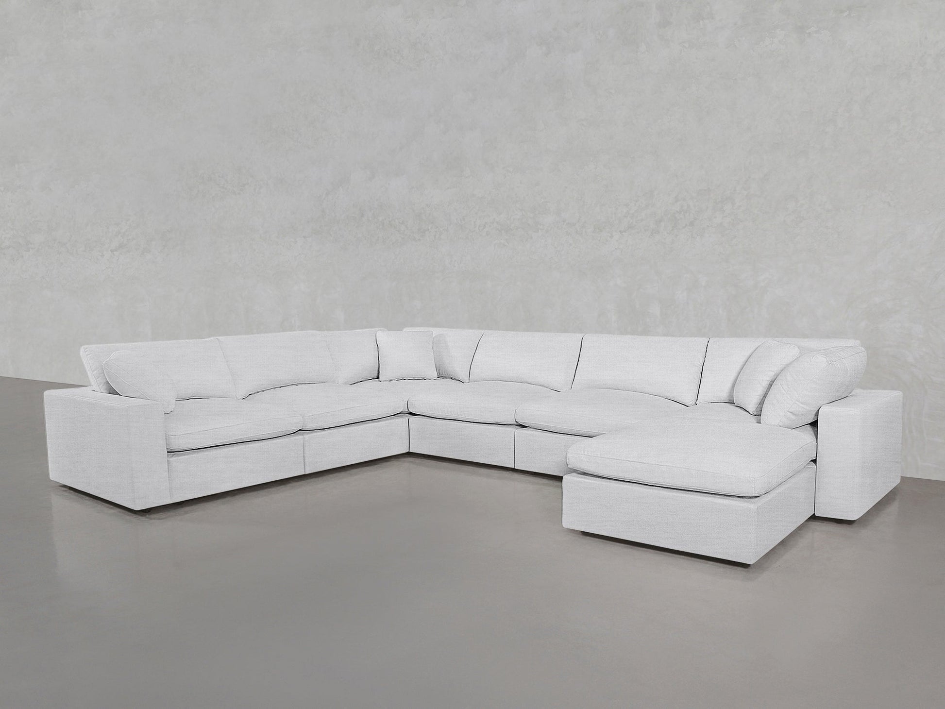 A spacious, modern white 7-Seat Modular Chaise Corner Sectional with a right-side chaise, set against light gray walls and flooring.