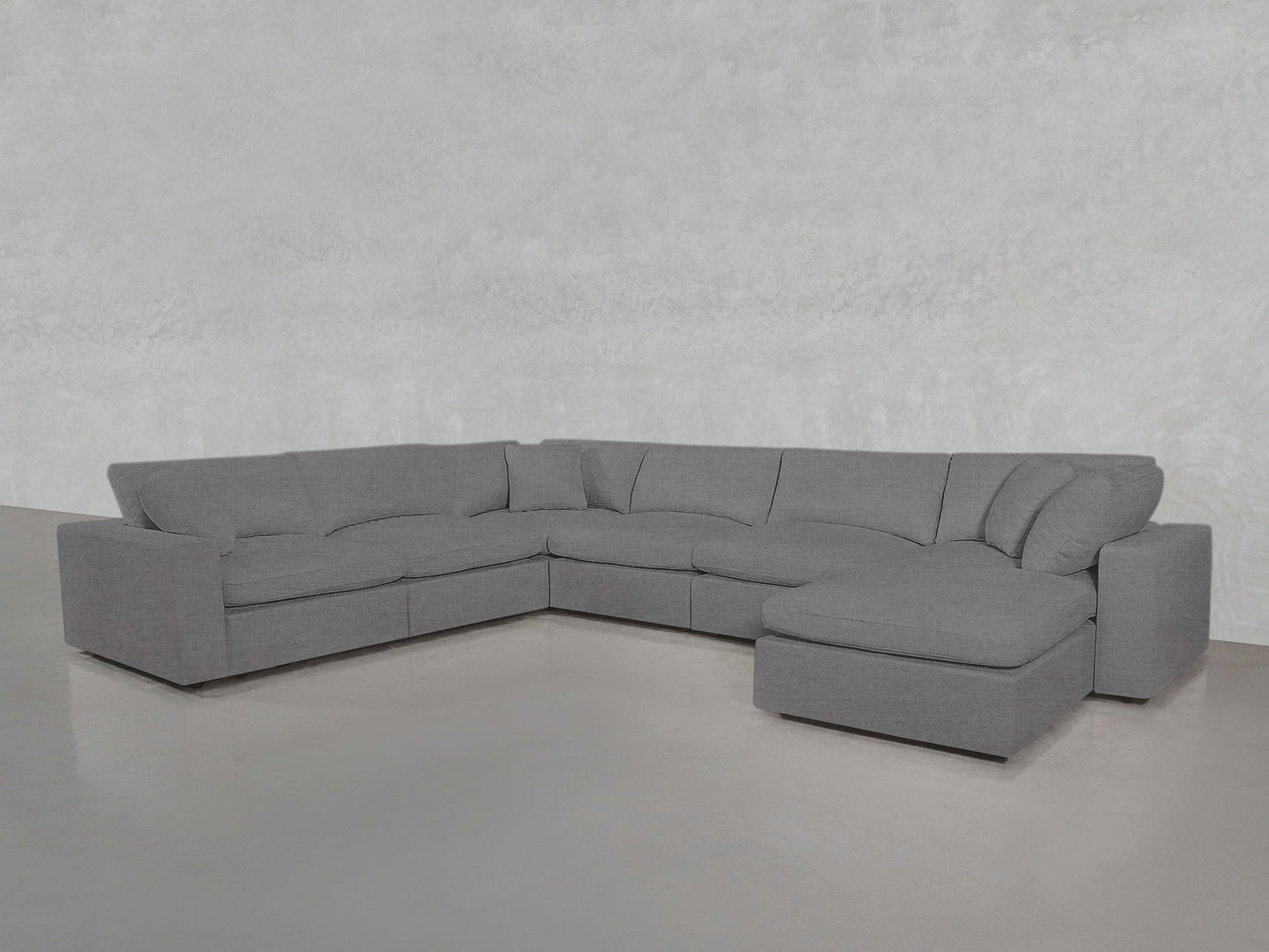 A spacious, modern 7-Seat Modular Chaise Corner Sectional with plush cushions and a right-side chaise is set in a minimalistic room featuring light gray walls and a smooth floor.