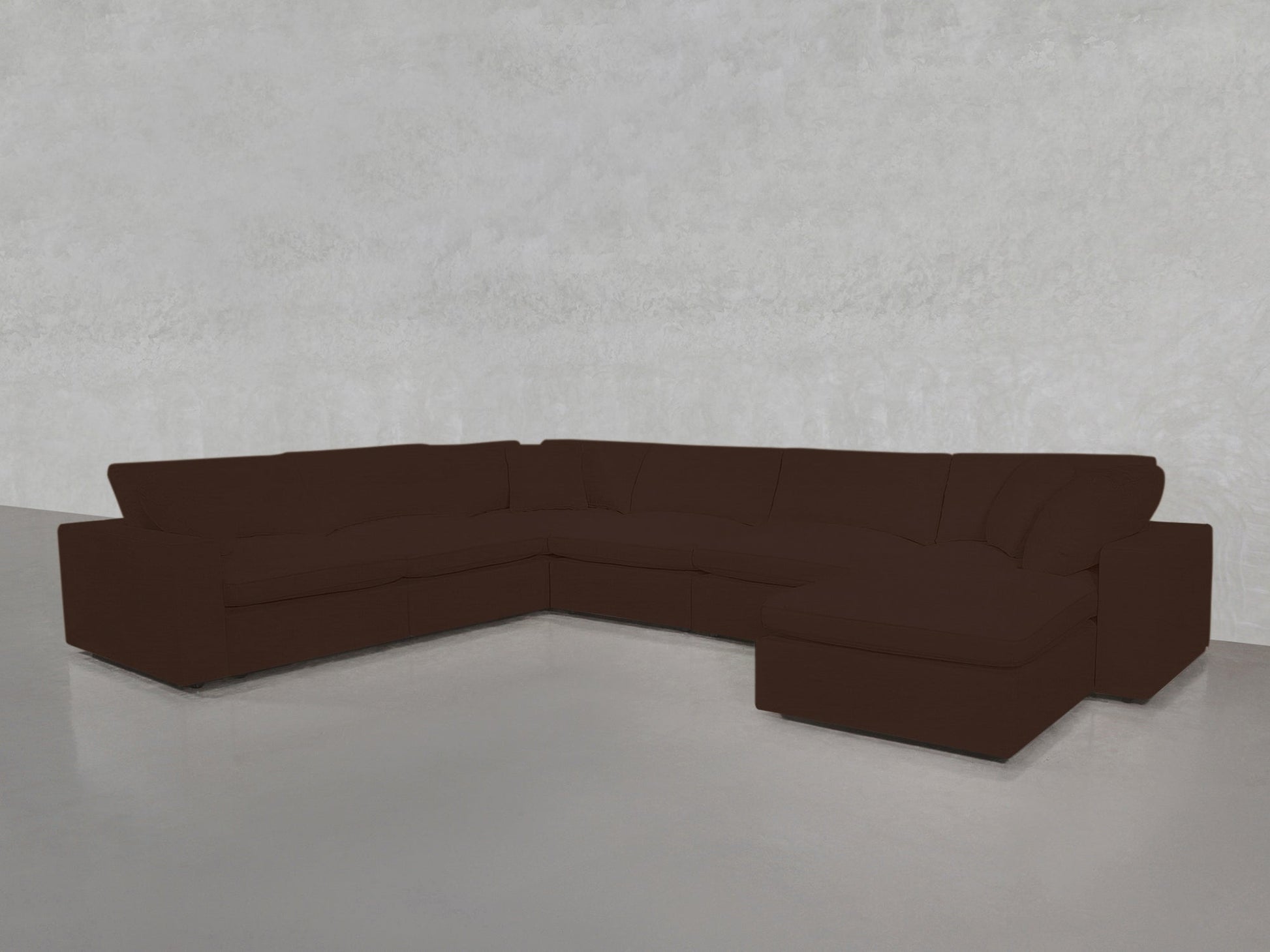 A spacious 7-Seat Modular Chaise Corner Sectional in dark brown, featuring plush cushions, sits in an empty room with light gray walls and a smooth, light floor.