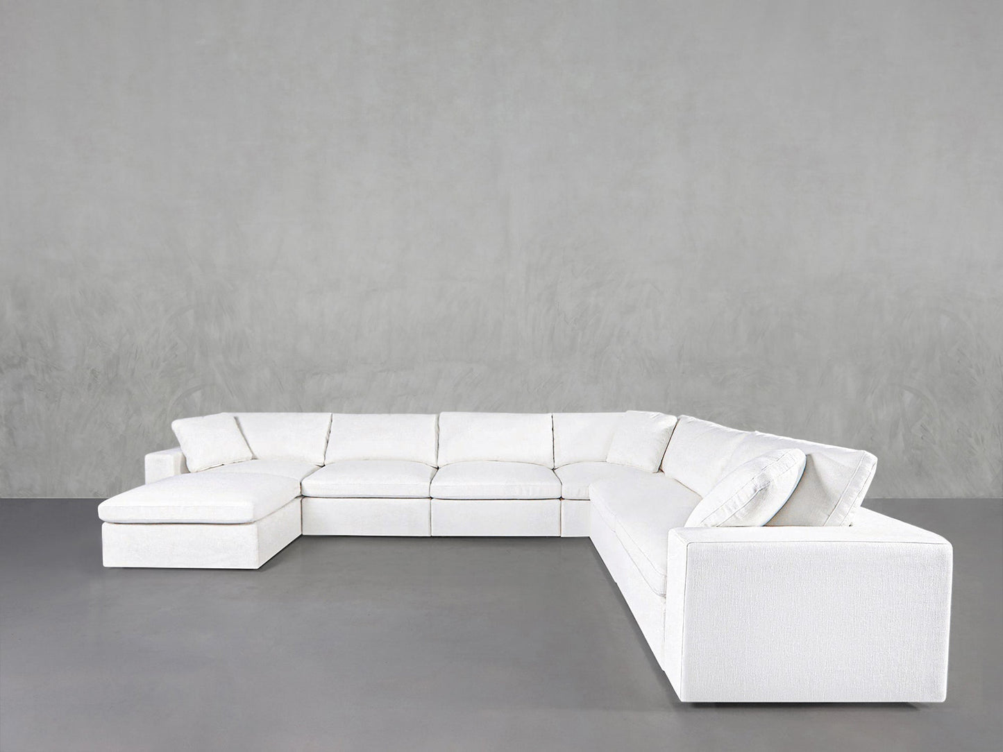 A 7-Seat Modular Chaise Corner Sectional in modern white sits against a plain light gray wall and floor, creating a spacious, minimalist look.