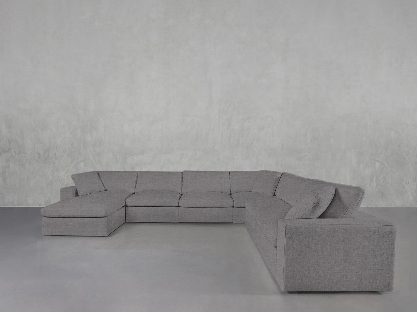 The 7-Seat Modular Chaise Corner Sectional with clean, modern lines is arranged on a smooth, light gray floor and set against a textured, light gray wall.