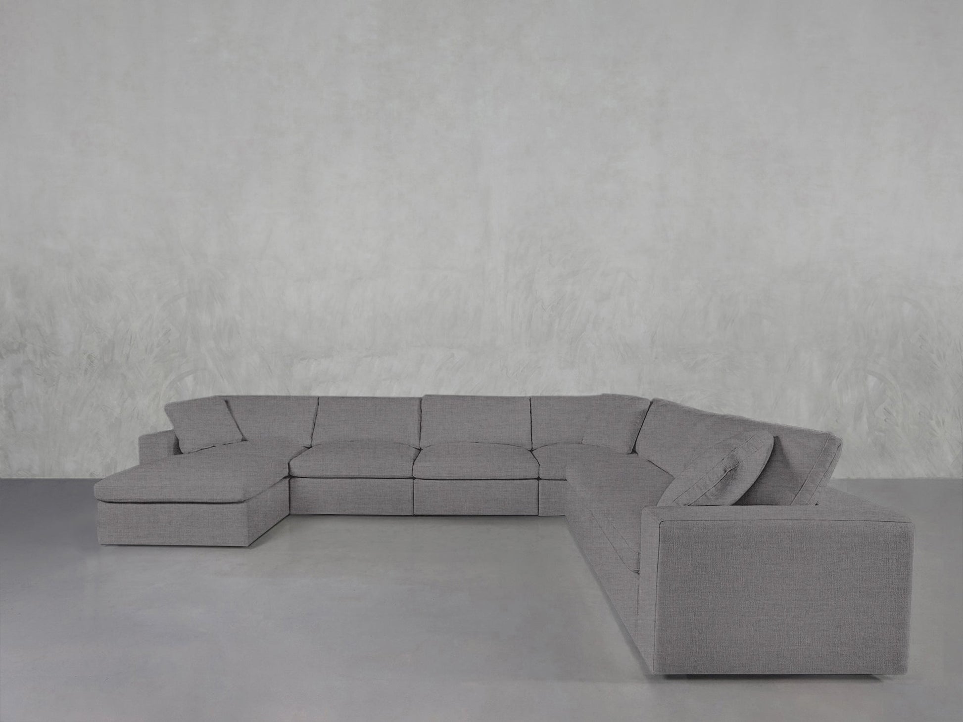 The 7-Seat Modular Chaise Corner Sectional with clean, modern lines is arranged on a smooth, light gray floor and set against a textured, light gray wall.
