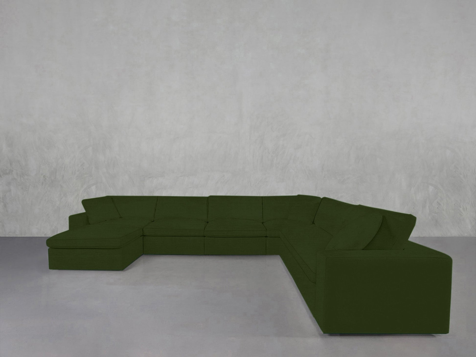 A 7-Seat Modular Chaise Corner Sectional in dark green stands against a textured light gray wall on a smooth, light gray floor, adding clean lines to the minimalist room.