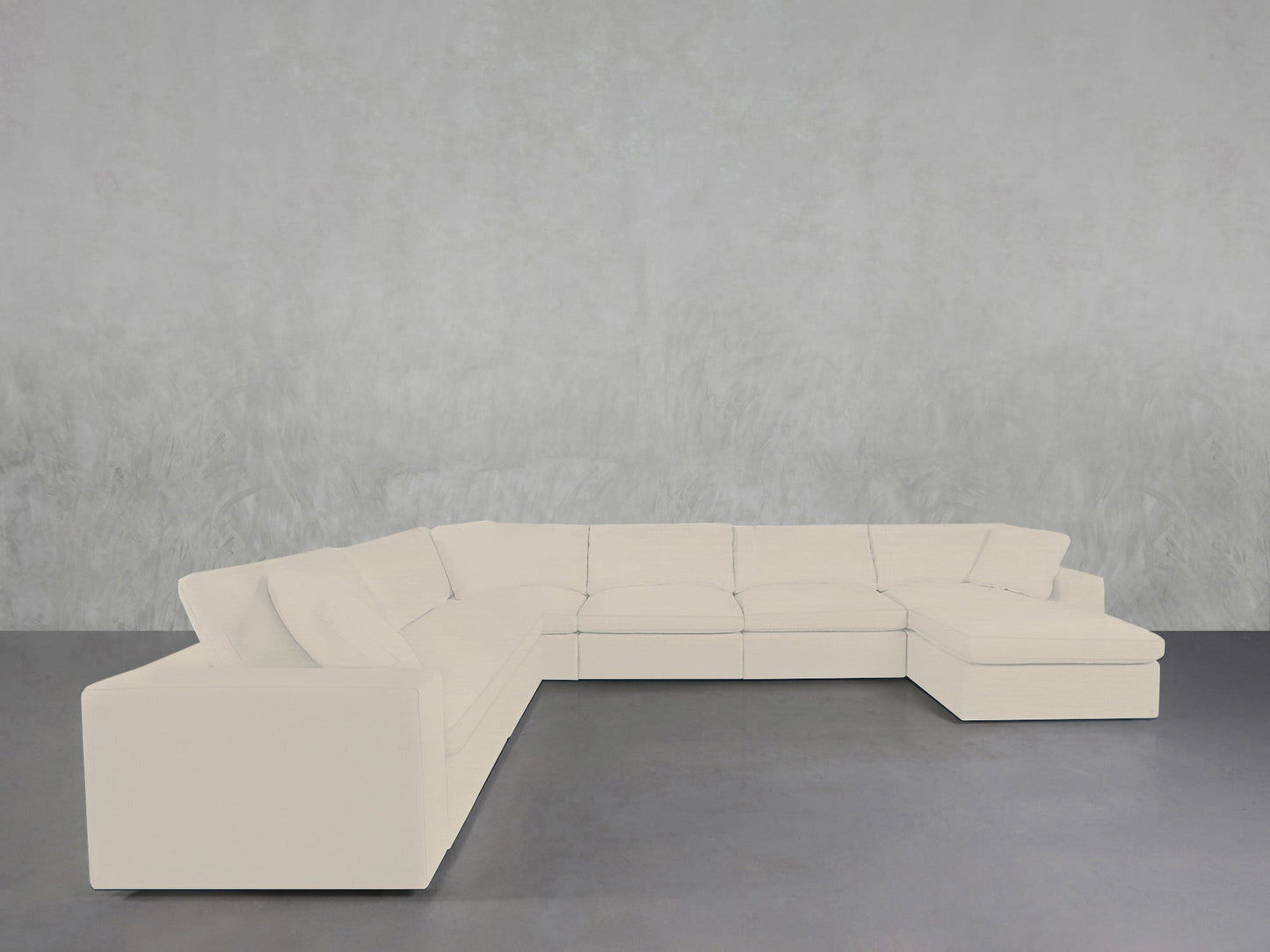 A 7-Seat Modular Chaise Corner Sectional in white is arranged in a minimalist room featuring a gray textured wall and a dark gray floor.
