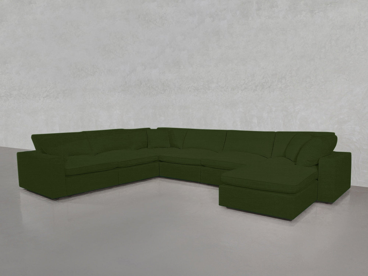 A spacious 7-Seat Modular Chaise Corner Sectional in dark green, featuring plush cushions, sits in a minimal light gray room with smooth floors and a textured wall.