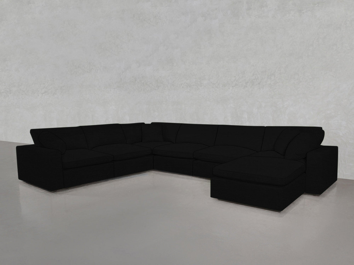 A spacious 7-Seat Modular Chaise Corner Sectional in black with plush cushions sits in the corner of a minimalist room featuring light gray walls and a smooth, light-colored floor.