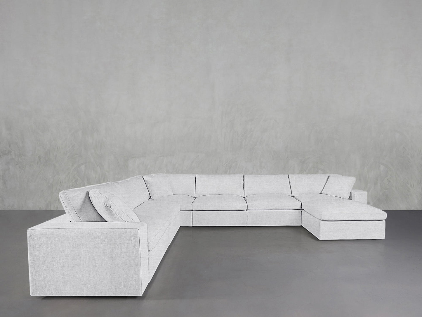 A 7-Seat Modular Chaise Corner Sectional in light gray is placed in an empty room with a plain gray textured wall and a smooth gray floor.