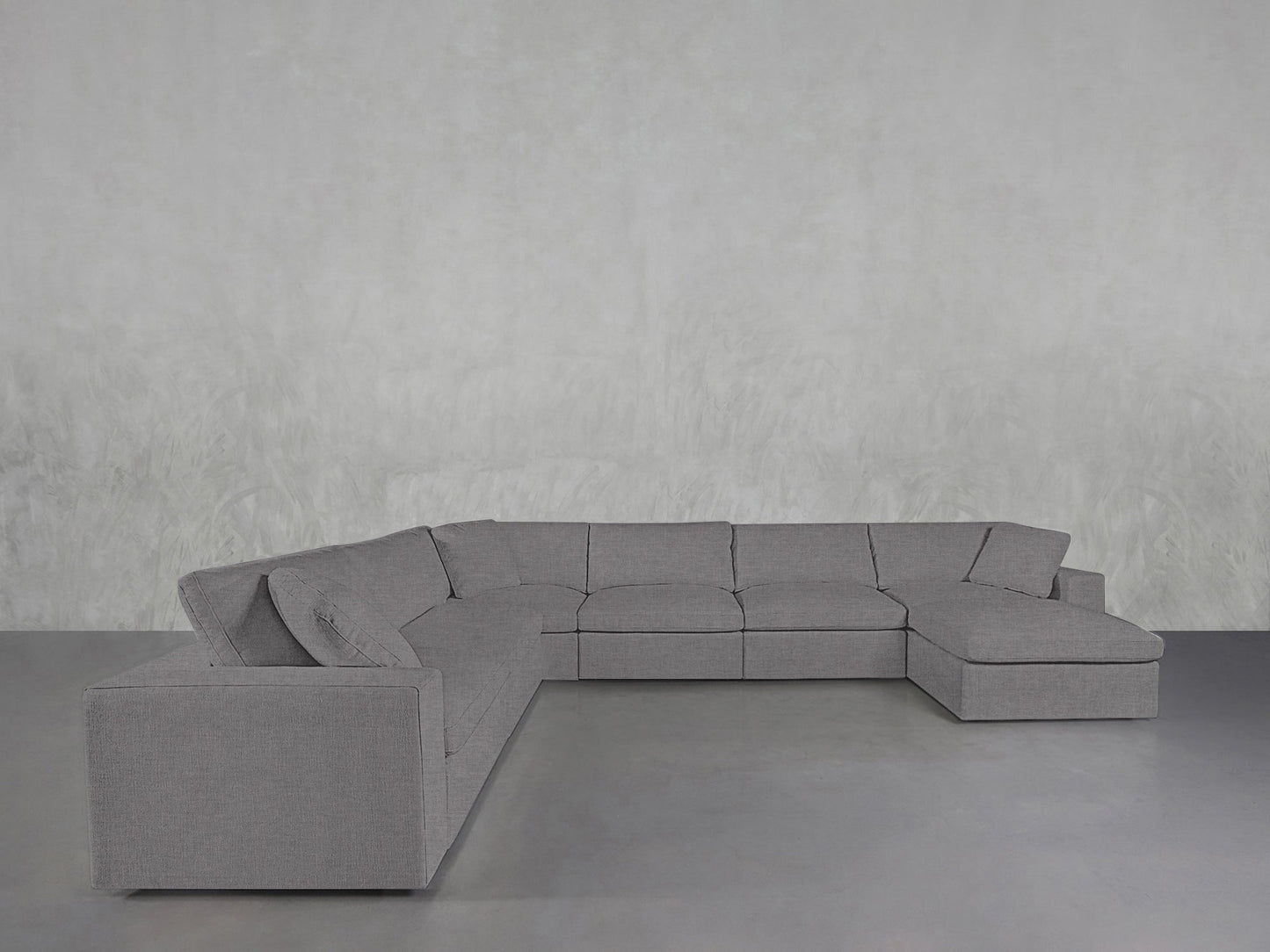 A spacious 7-Seat Modular Chaise Corner Sectional in modern grey is placed in an empty room with light grey textured walls and a smooth grey floor, featuring a right-side chaise lounge.
