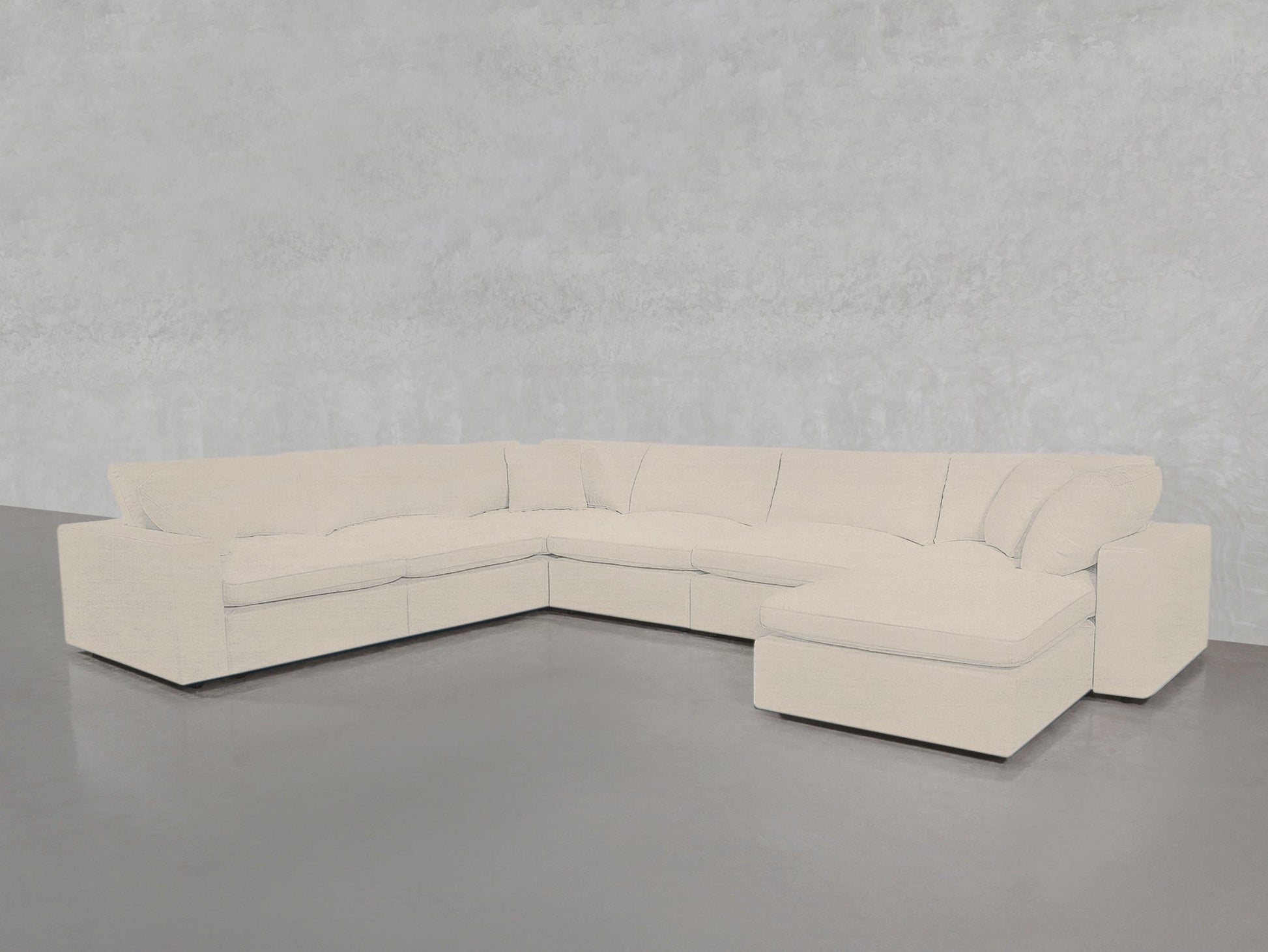 A 7-Seat Modular Chaise Corner Sectional in light beige with plush cushions sits on a gray concrete floor against a textured light gray wall.