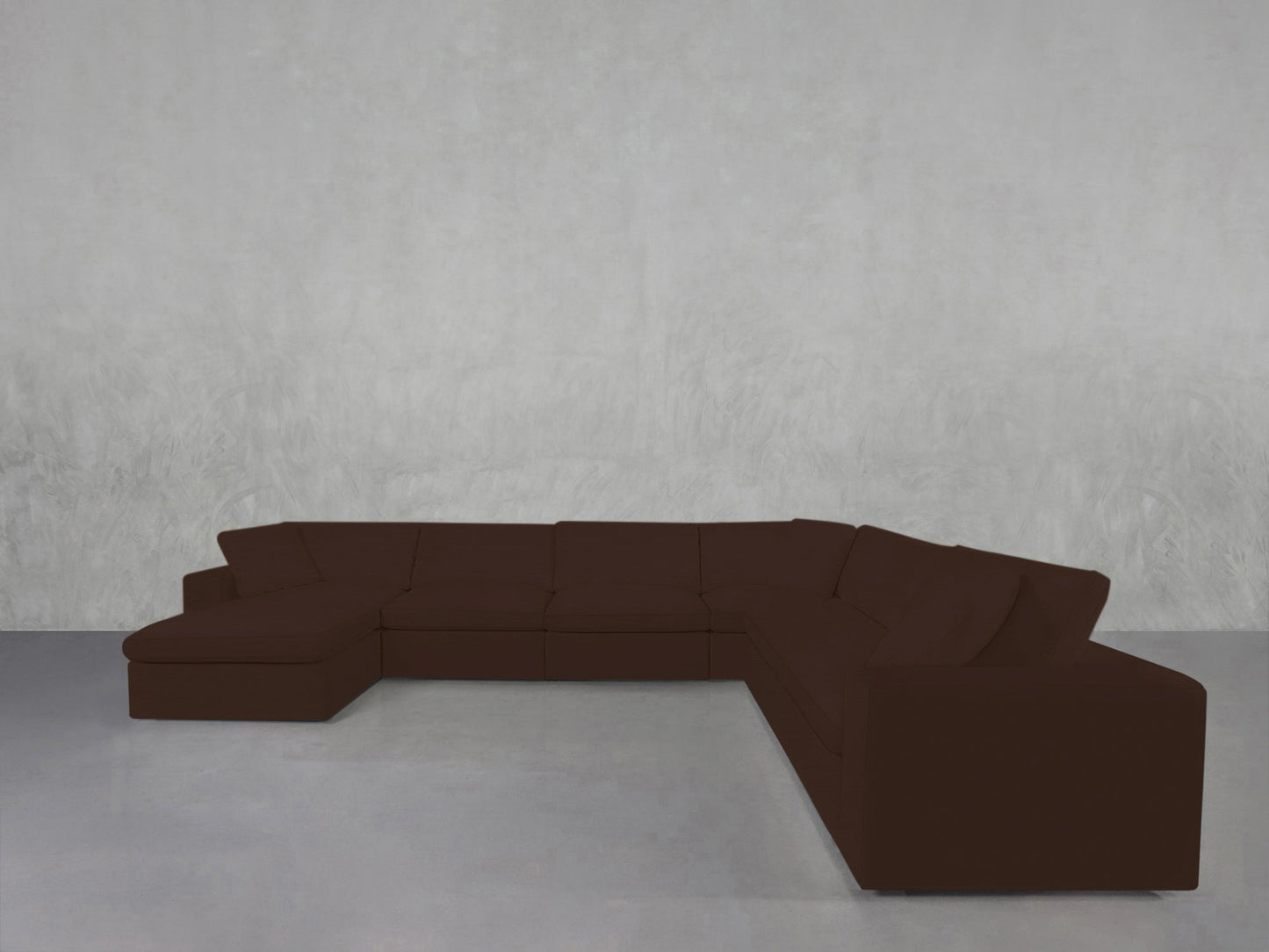 A 7-Seat Modular Chaise Corner Sectional with a chaise lounge on the left is placed against a plain, light gray textured wall and floor in an empty room.