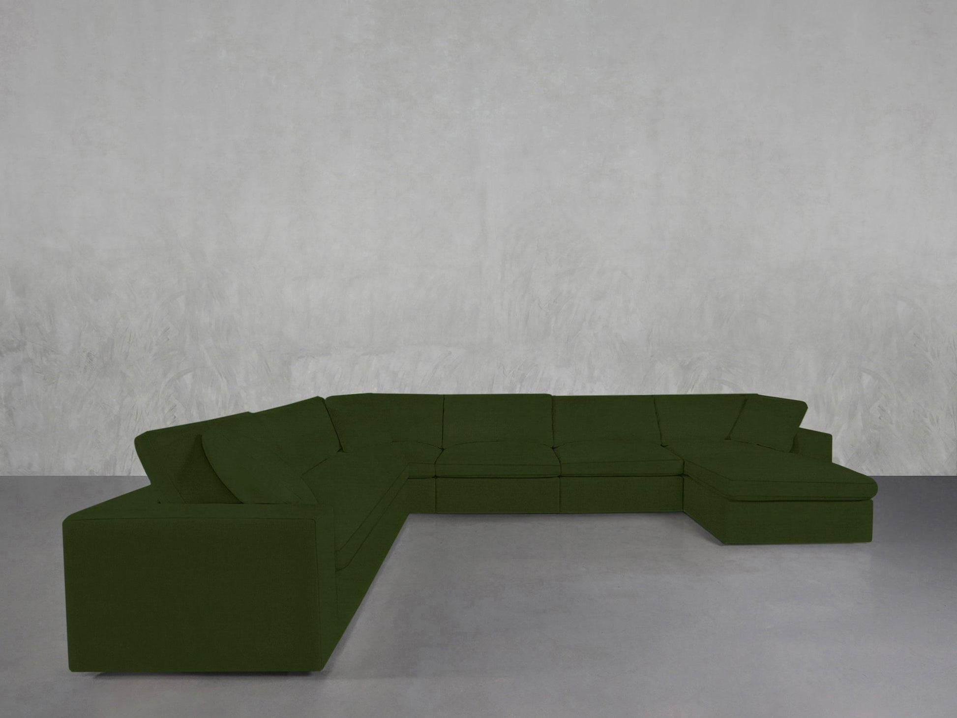 A 7-Seat Modular Chaise Corner Sectional in dark green rests on a smooth grey floor against a light grey textured wall, creating a minimal, modern setting that highlights the sleek sectional.