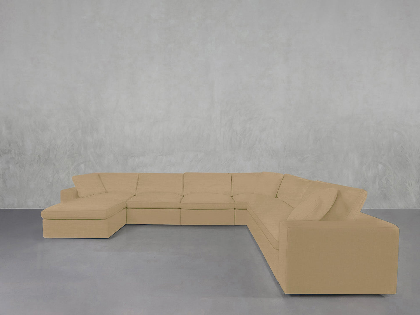 A 7-Seat Modular Chaise Corner Sectional with cushions is arranged in an L-shape against a light gray textured wall on a smooth gray floor.