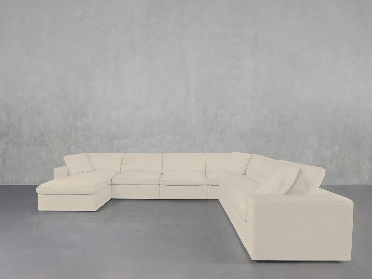 A 7-Seat Modular Chaise Corner Sectional in white sits on a gray floor against a light gray textured wall, creating a minimalist and spacious atmosphere.