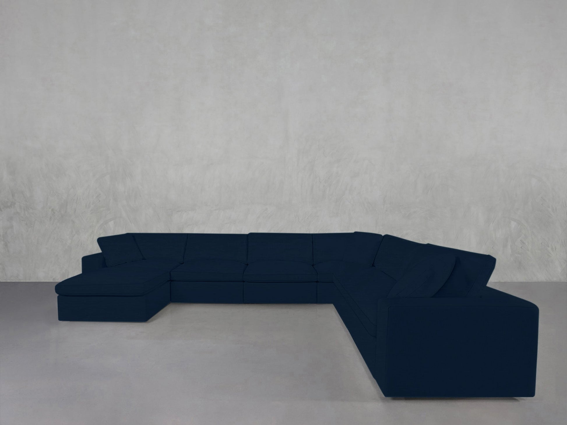 A spacious 7-Seat Modular Chaise Corner Sectional in dark blue, featuring wide seats and low backs, sits in an empty room with light gray walls and a smooth, light floor.