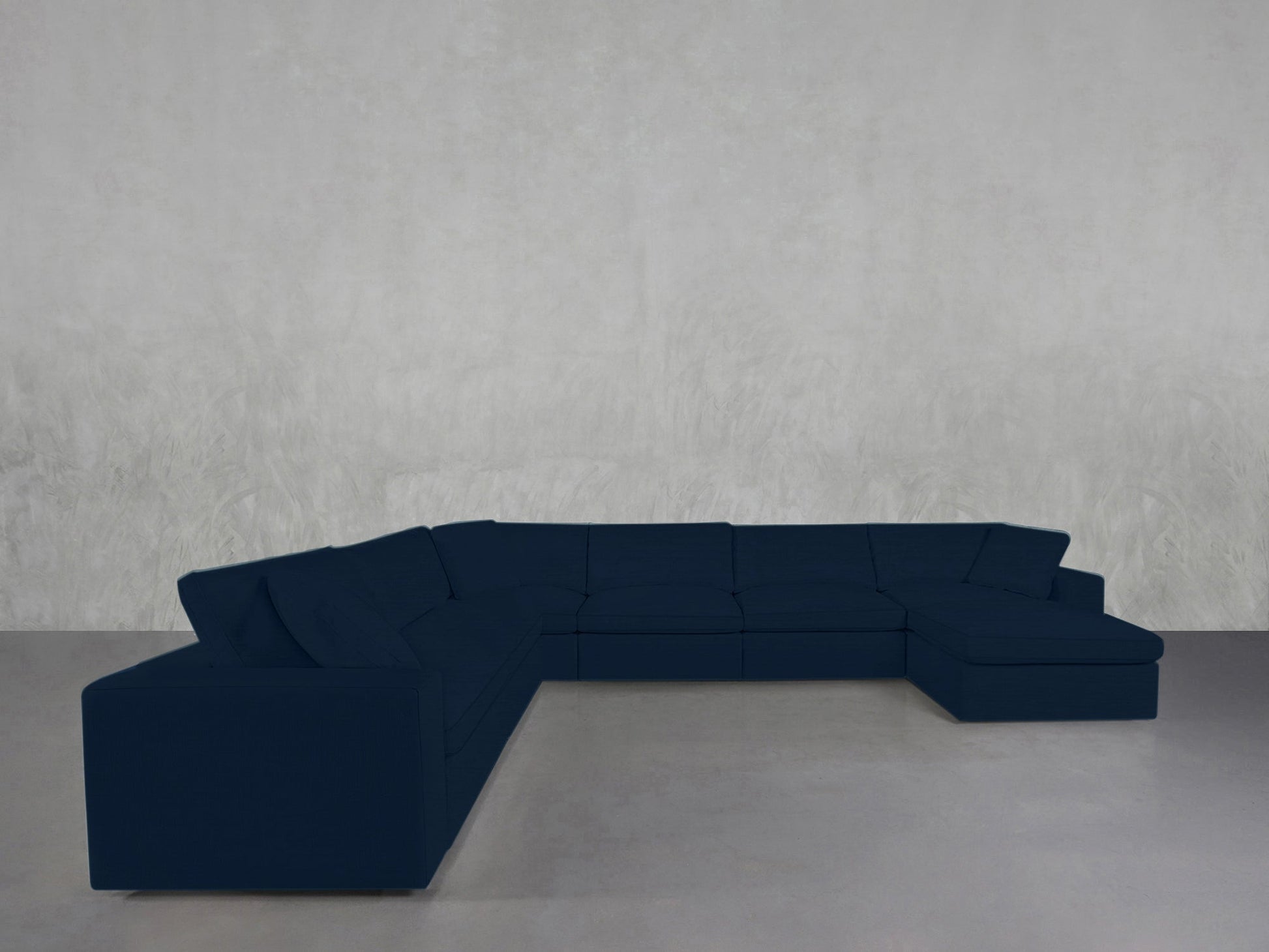 A 7-Seat Modular Chaise Corner Sectional in dark blue is placed in the corner of a room with light gray walls and a smooth, light gray floor.