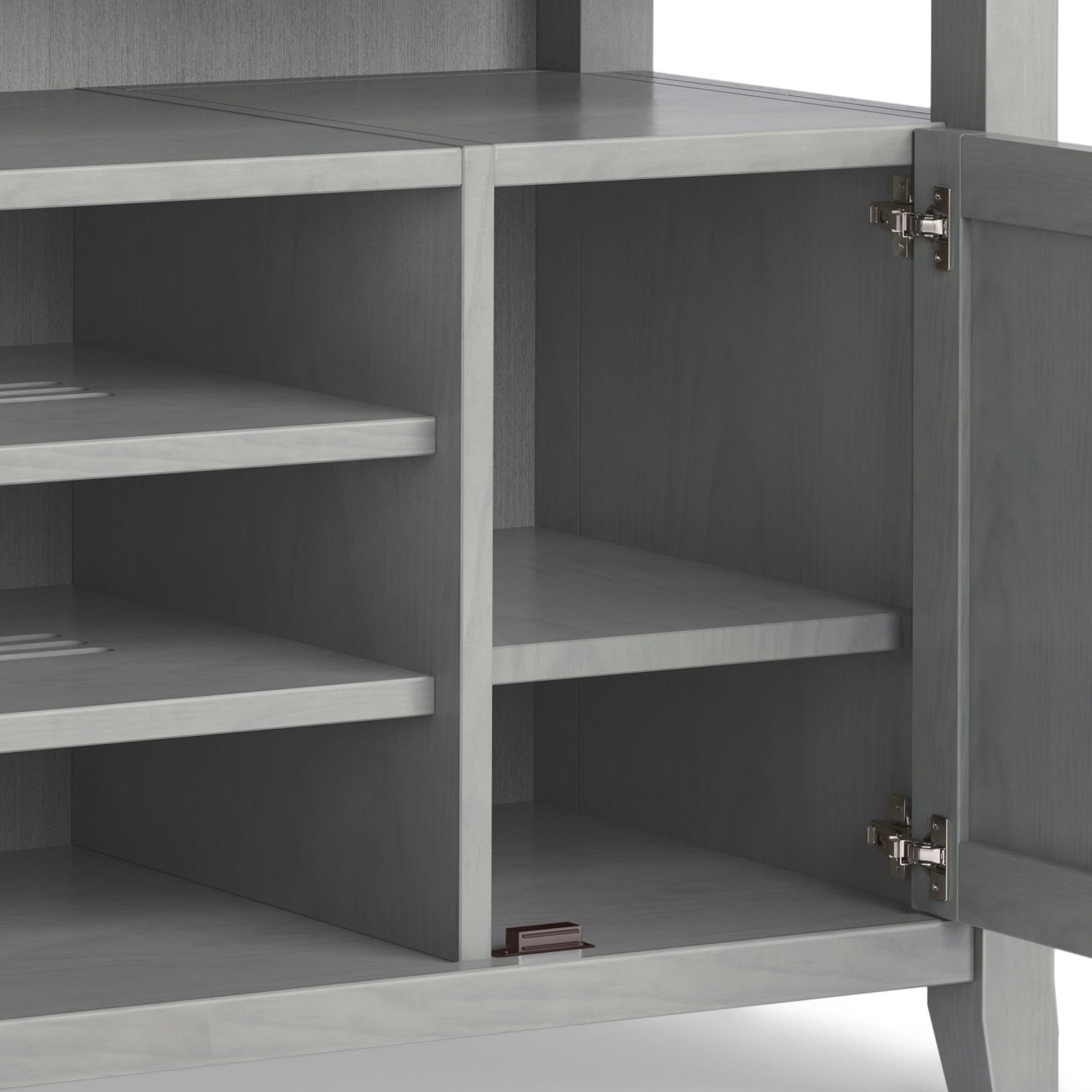 The Amherst TV Media Stand, handcrafted in gray wood, features an open cabinet with two interior shelves, metal door hinges, and a small brown rectangular object on the bottom shelf.
