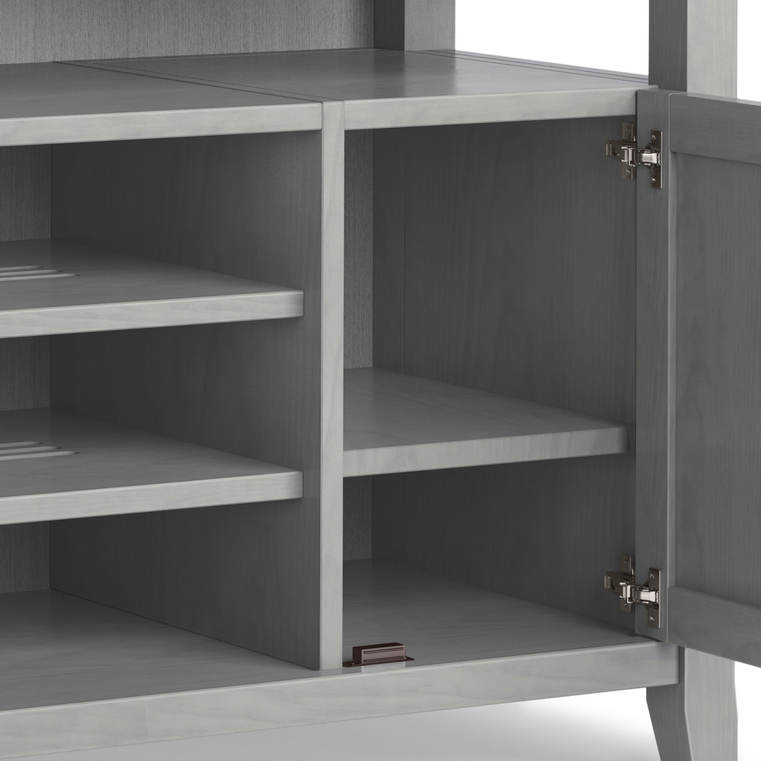 The Amherst TV Media Stand, handcrafted in gray wood, features an open cabinet with two interior shelves, metal door hinges, and a small brown rectangular object on the bottom shelf.