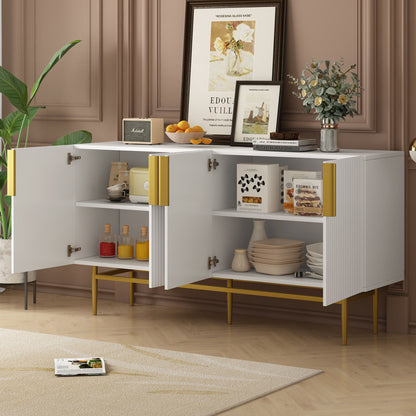 The Modern Elegant 4 Door Sideboard Gold Metal Handle Buffet Cabinet stands against a brown paneled wall with its doors open, displaying dishes, jars, and cookbooks. Art, flowers, and fruit decorate the top, while a plant is placed nearby.