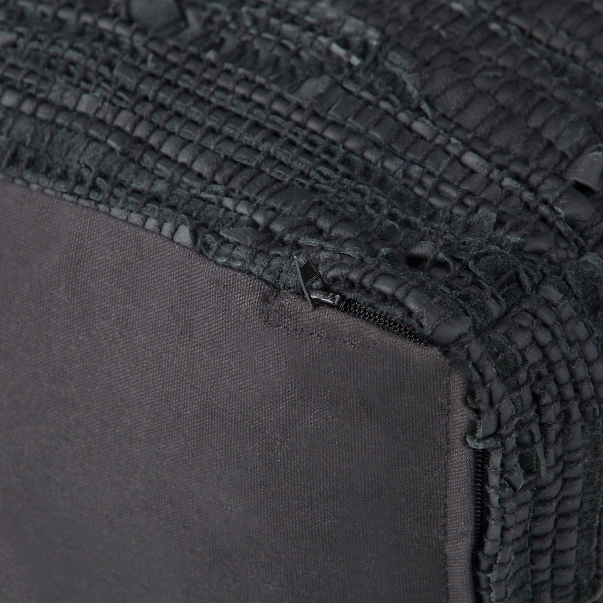 Close-up of the Fredrik - Handcrafted Square Pouf in black fabric, featuring a textured, woven corner, visible stitching, and a partially exposed zipper near the seam.
