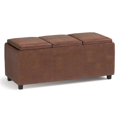 The Avalon - Upholstered Storage Ottoman is a rectangular brown leather piece with three cushioned lids and short black legs, shown against a white background.