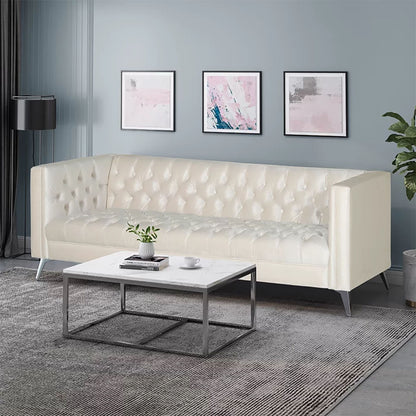 A modern living room featuring the Contemporary 3 Seater Sofa With Button Tufting in cream, a white marble coffee table with a plant and books, gray rug, three abstract pink and gray wall art pieces, and a black floor lamp against blue-gray walls.