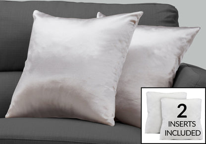 Two light gray satin decorative throw pillows from Modern come with two white, hypoallergenic inserts. The square pillows are displayed on a dark gray sofa. Text inset: "2 INSERTS INCLUDED.