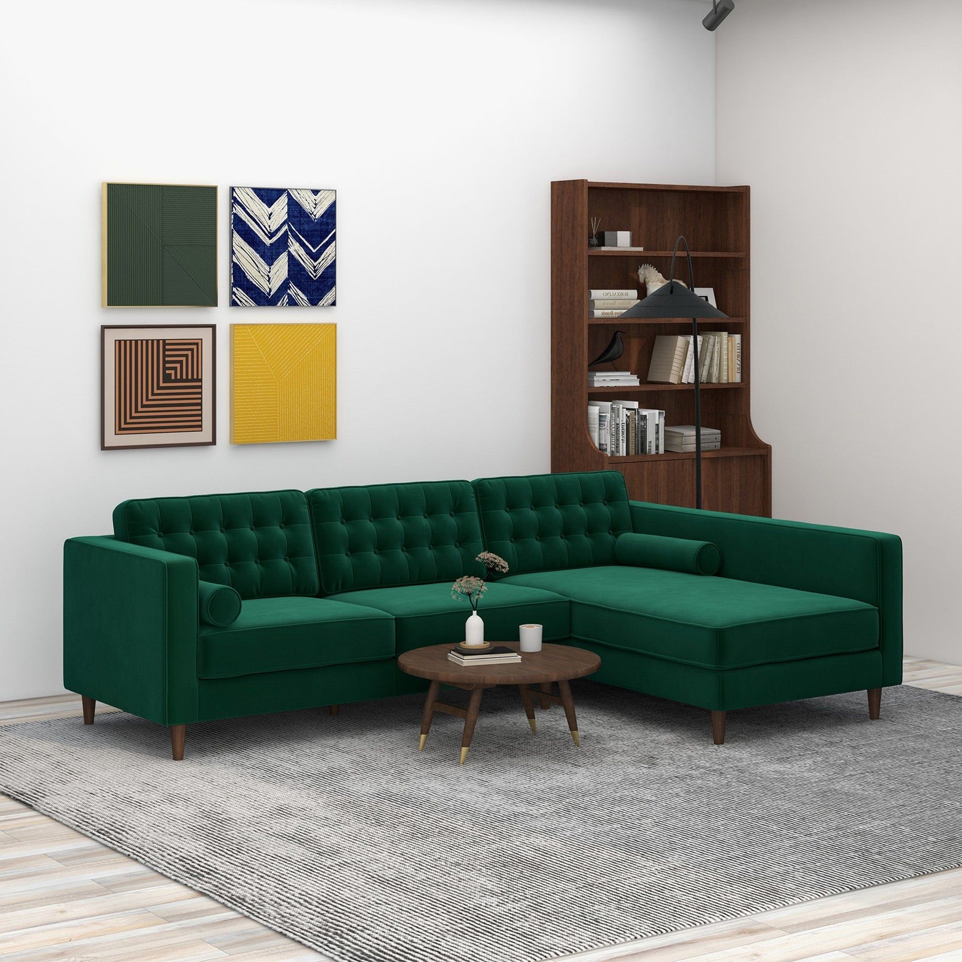 A modern living room featuring the Christian Mid-Century Modern Design Sectional Sofa in green, a round wooden coffee table, gray rug, bookshelf with books, and four colorful geometric art pieces on a white wall.