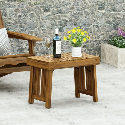 The Temptation Outdoor Foldable Side Table With Slat Design holds a bottle of wine, wine glass, and a white vase with yellow flowers. It's placed on a patio near a wooden chair and stone wall with greenery in the background.