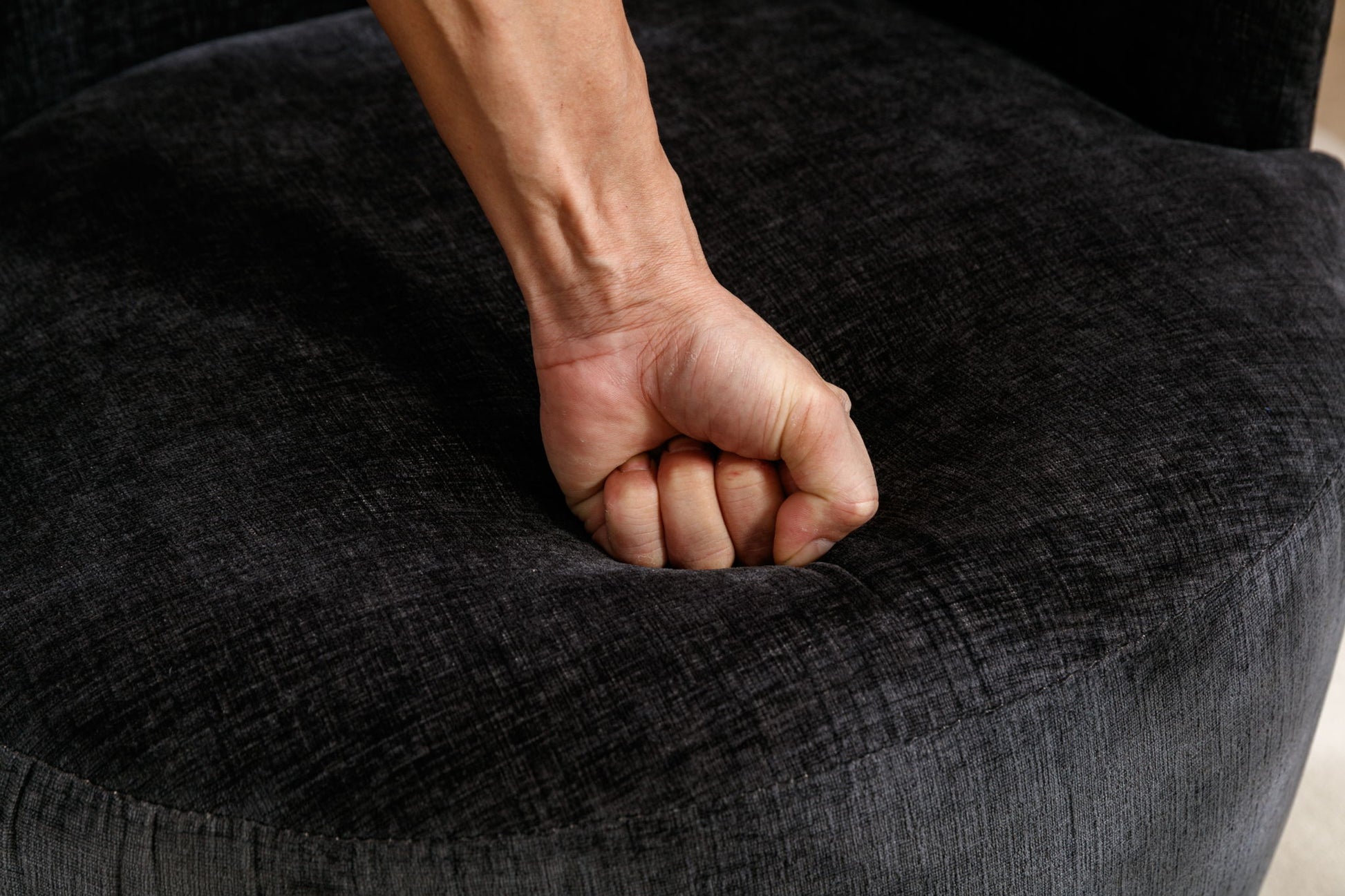 A close-up of a person’s fist pressing down on the Chenille Fabric Swivel Accent Armchair Barrel Chair With Powder Coating Metal Ring, creating a visible indentation in the dark gray, textured chenille fabric.