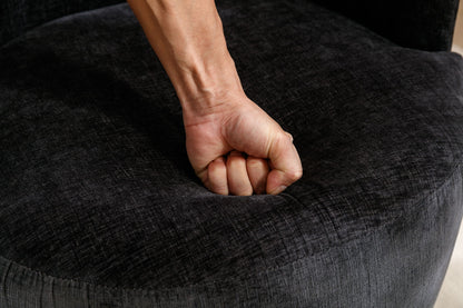 A close-up of a person’s fist pressing down on the Chenille Fabric Swivel Accent Armchair Barrel Chair With Powder Coating Metal Ring, creating a visible indentation in the dark gray, textured chenille fabric.