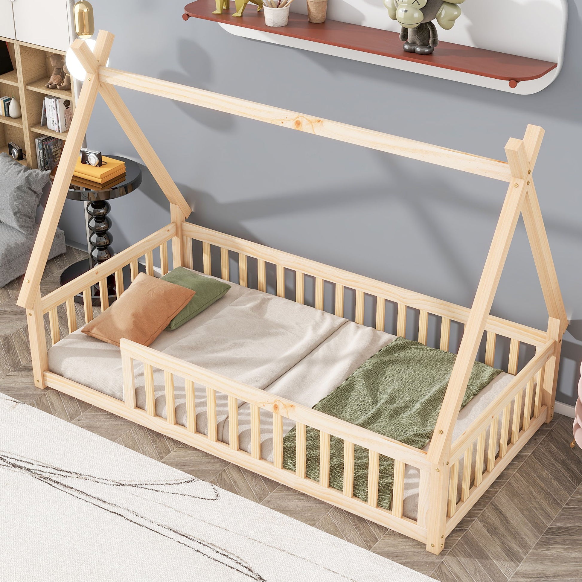 A Tent-Shaped Floor Bed, Teepee Bed with Guardrails and slats sits on a patterned rug in a cozy, modern kids’ room, decorated with pillows, a green blanket, shelves, and toys on the wall.