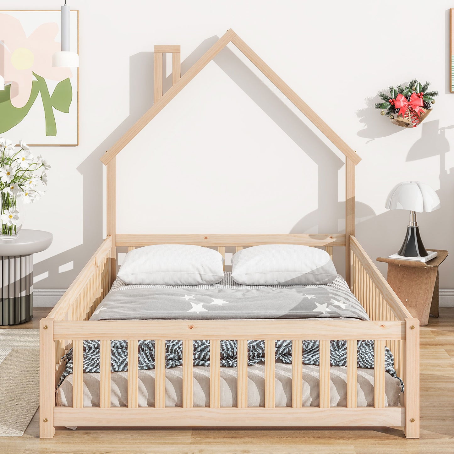 The room features a House-Shaped Headboard Floor Bed With Fence, dressed in white and gray bedding with two pillows and star patterns. Decor includes light walls, wall art, a small table with flowers, and a wreath.
