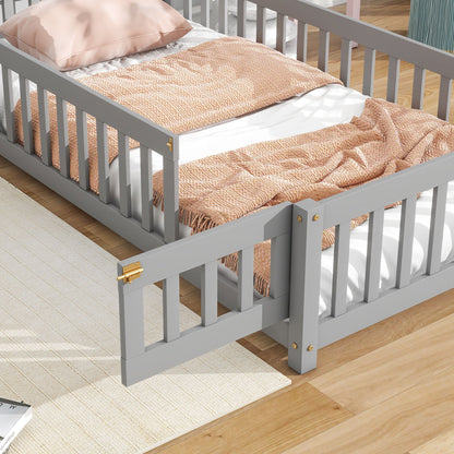 The House-Shaped Headboard Floor Bed With Fence, shown in gray with a partially open side gate, features a peach knitted blanket, white sheets, and a pink pillow. It stands on a light wood floor beside a beige rug.
