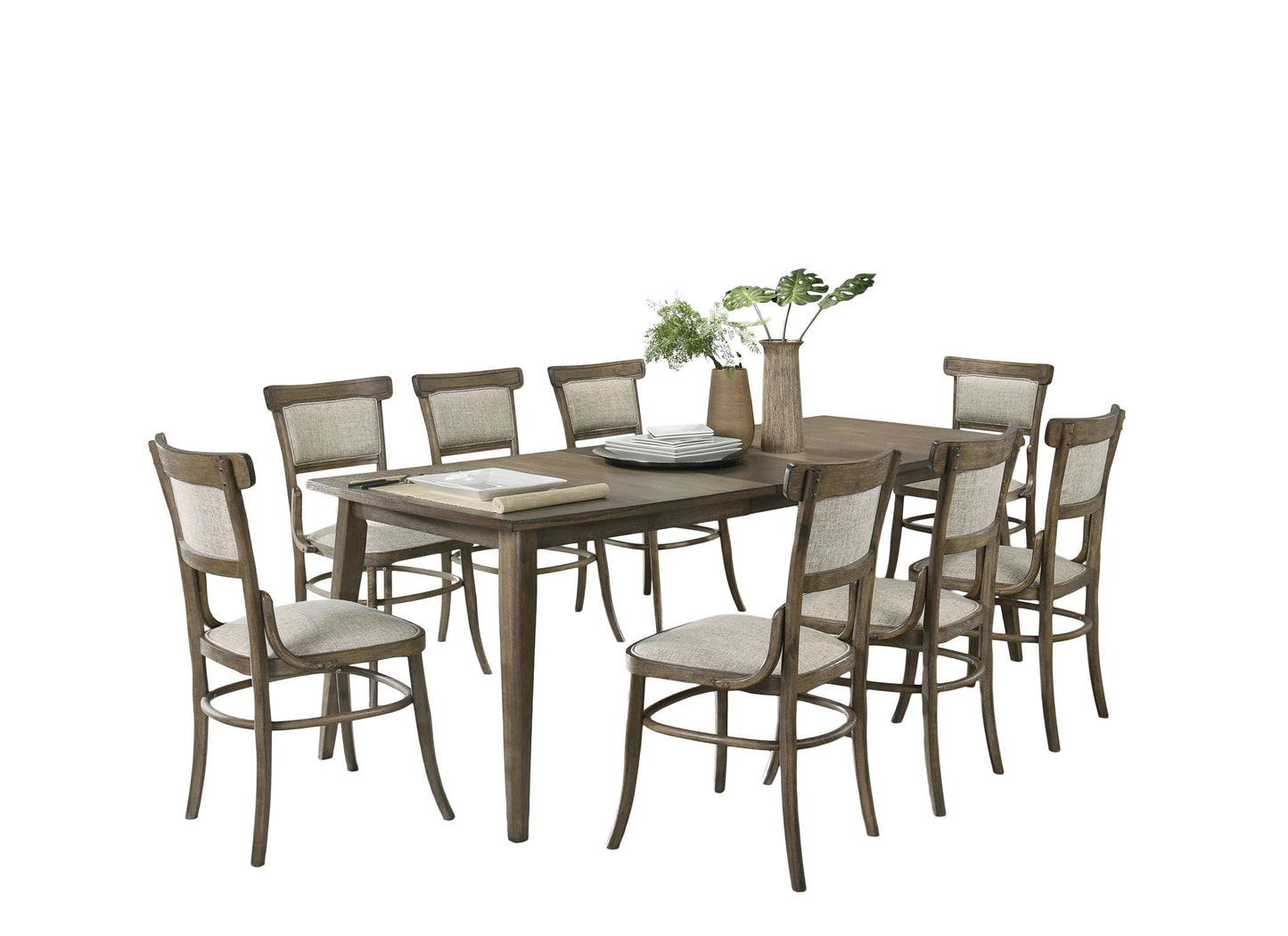 The Bistro Dining Table with Off White Fabric Dining Chairs set includes a wooden table and eight matching chairs with upholstered seats and backs. The table is styled with stacked plates, books, and a vase of green plants against a plain white background.