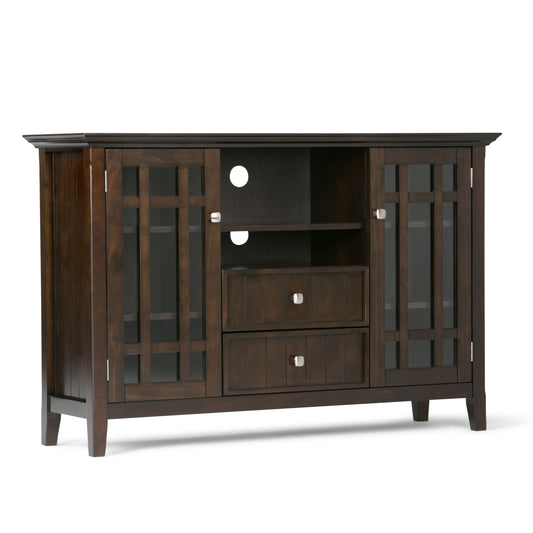 The Bedford Handcrafted Tall TV Media Stand features dark brown wood, glass-paneled doors on each side, two center open shelves with cable holes, two drawers below, four legs, and square metal handles.