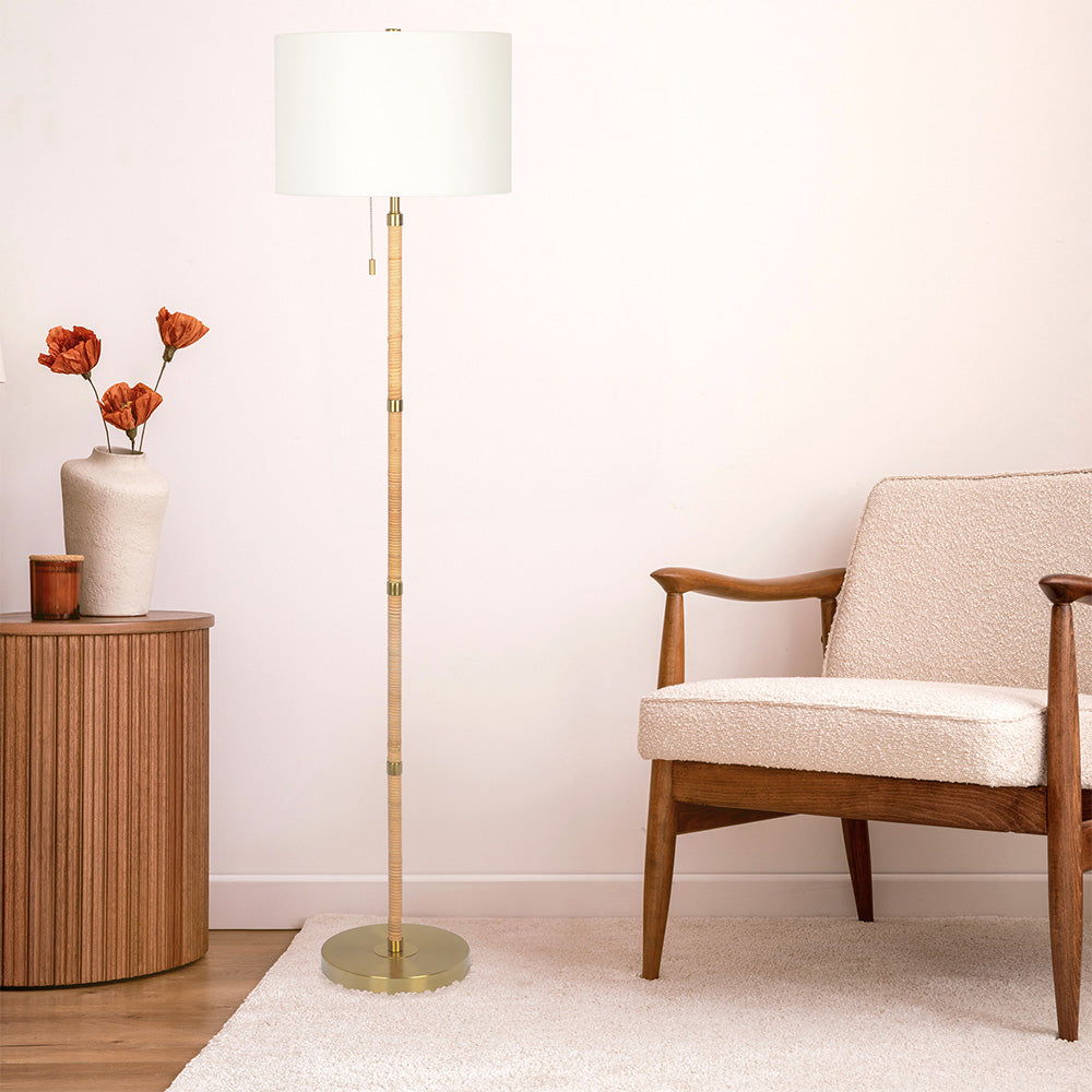 A cozy living room corner with a wooden armchair, a round side table, a vase of dried flowers, a light rug on wooden floors, and the Stellar Linen Shade Floor Lamp in Gold/Natural Wood/Rattan/White.