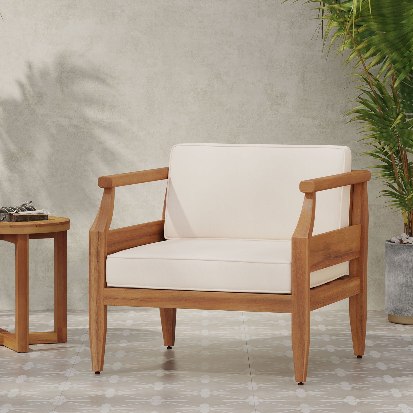 An Outdoor Club Chair With Recessed Arms And Cushions sits on a tiled floor beside a small wooden side table and a tall potted plant, placed against a light-colored wall.
