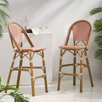 Two Outdoor Pe Rattan French Barstools with brown and white checkered seats and backs are placed by a white stone pedestal adorned with glasses and a bottle, while green plants frame the sunlit space.