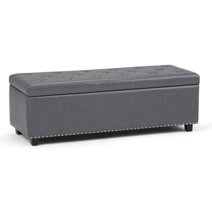 The Hamilton Upholstered Storage Ottoman features a rectangular, dark gray tufted design with short black legs and silver nailhead trim along the base, offering stylish storage for any space.